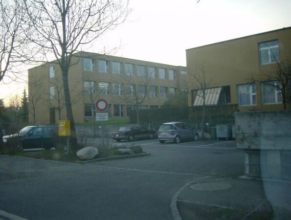 Parkplatz vor dem Schulhaus Junkholz, dahinter das Schulgebäude.