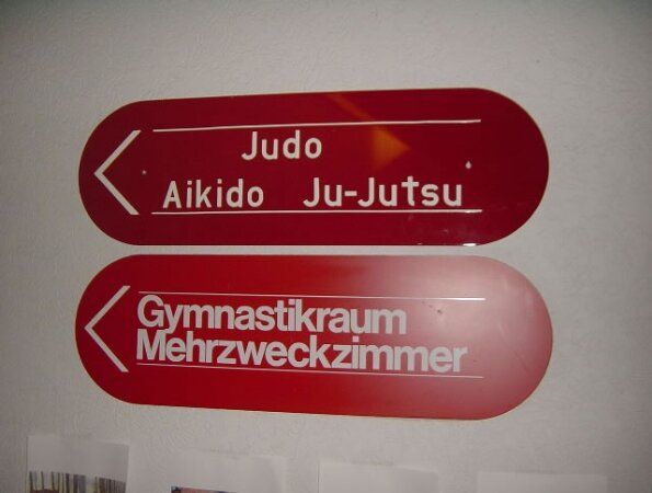 Rotes Wegschild mit Pfeil nach links: Judo, Aikido, Ju-Jutsu.