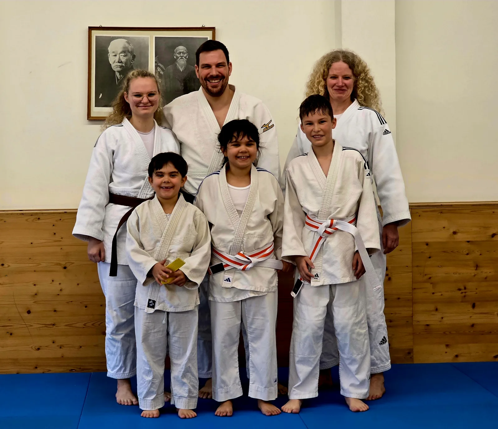 Gruppenfoto mit drei Kindern in Judogi vorne und drei Erwachsenen hinten in der Turnhalle auf der Matte.